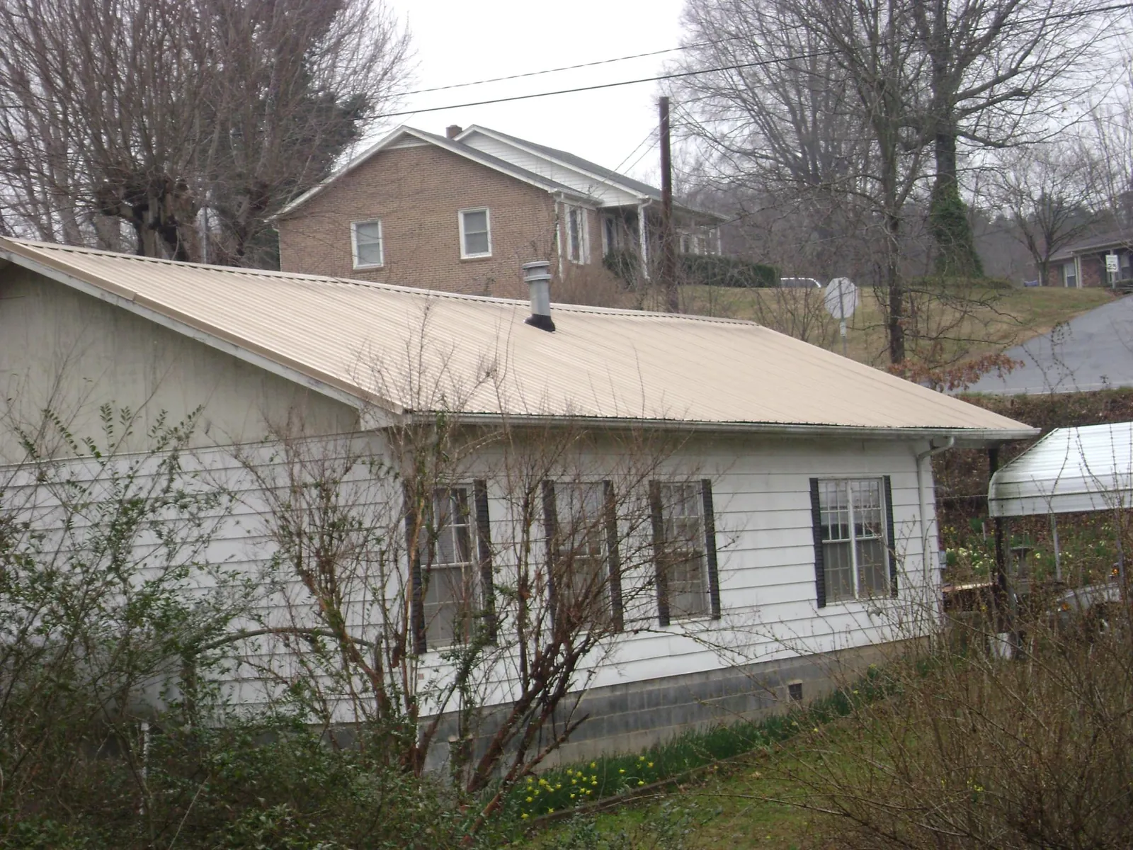 Tan metal roof on a white sided house set into a hillside — Commercial Roofing by Roofing Brothers in Ewa Beach